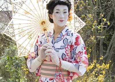 Person wearing traditional Japanese attire, including a floral kimono and holding a parasol, stands outdoors.