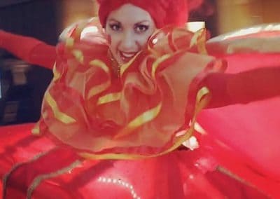Person in a vibrant red costume with gold accents, featuring a large headpiece. The outfit has ruffles and an expansive skirt, suggesting dynamic movement.